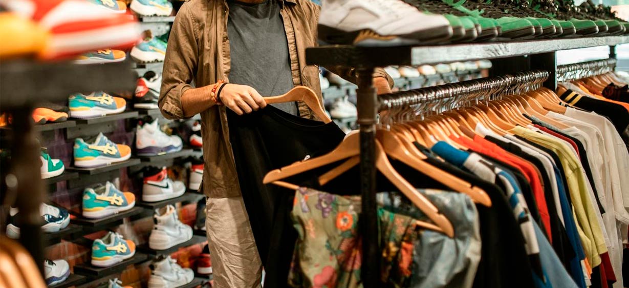 Vemos a una persona mirando ropra en una tienda deportiva. Tiene en la mano una camiseta con su percha